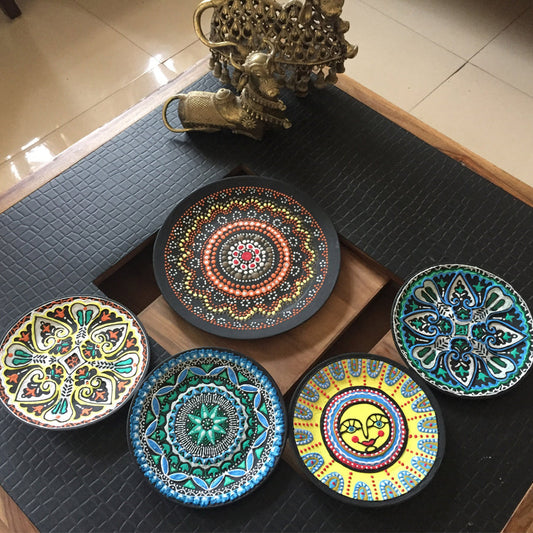 Set of colorful decorative plates on a black mat with a gold statue in the background.